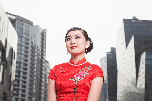 Beautiful young Asian woman in red Chinese dress traditional cheongsam qipao with gesture of congratulation and happy smiling face, she standing in front of the ancient wall (Chinese new year concept)