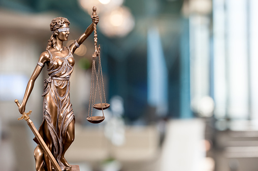 A bronze statue of the Lady Of Justice  composited into a blur background of a law firm.