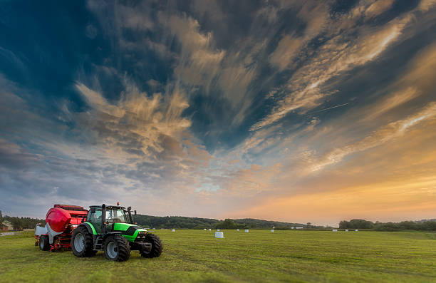 trattore alla luce del tramonto con palline di insilato sullo sfondo - hay wheat bale stacking foto e immagini stock