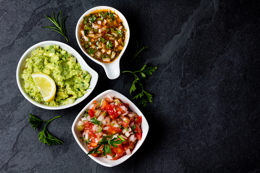 Traditional mexican Latin American sauces - avocado sauce Guacamole, tomato sauce Salsa, chili sauce Pebre in white bowls on stone slate background