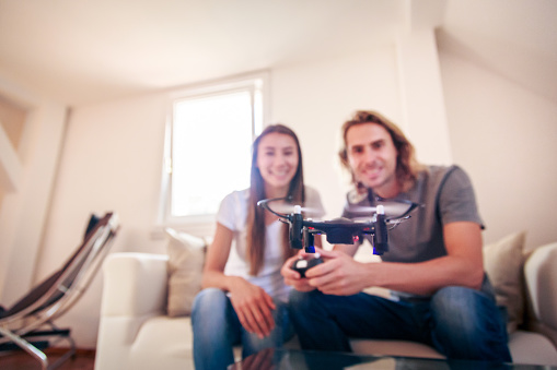 Young couple playing with a small quadrocopter drone at home in their living room.