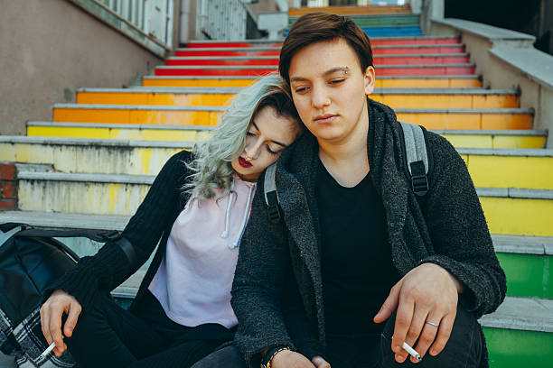 Sad urban lesbian couple enjoy Same sex young female real couple hanging out and embracing on colorful stairs in Istanbul. Looking sadly with cigarettes gay long hair stock pictures, royalty-free photos & images