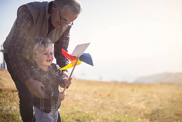 Grandfather and grandson having wonderful day at mountain.They play with colourful pinwheel.