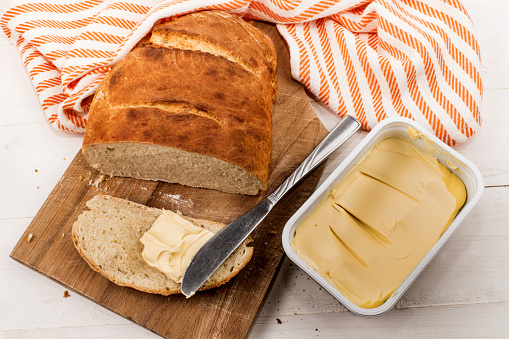 slice home baked bread with margarine and knife on a cutting board
