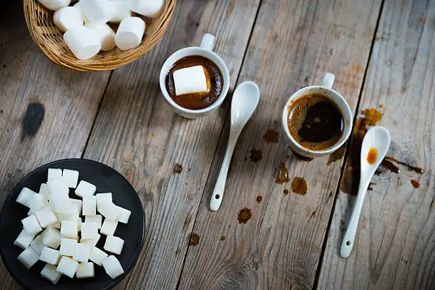 Two cups of hot coffee with marshmallows and cookies on wooden background, top view, close up.