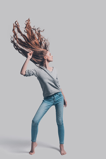 Full length studio shot of attractive young woman with tousled hair posing against grey background