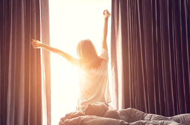 женщина растяжения возле кровати после пробуждения - waking up window women morning стоковые фото и изображения