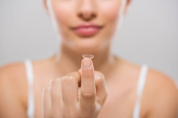 Woman holding contact lens Focus on contact lens on finger of young woman. Young woman holding contact lens on finger in front of her face. Woman holding contact lens on grey background. Eyesight and eyecare concept. contact lens stock pictures, royalty-free photos & images