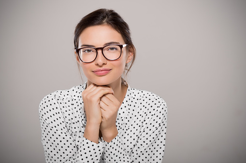 Young woman wearing modern eyeglasses anf thinking isolated on grey background with copy space. Portrait of smiling fashion student wearing big glasses. Proud young businesswoman with spectacles looking at camera.