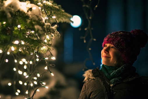 Little girl looking at the illuminated christmas tree outdoors during night. The girl is smiling at the beautiful lights on the tree.