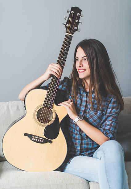 istock Young woman on sofa holding guitar 618976880