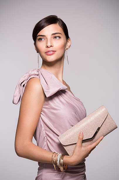 Elegant and fashion woman Young beautiful woman in elegant pink dress holding clutch and looking away. Fashion chic woman with purse ready for party. Portrait of elegant girl with luxury accessory isolated on background pink gown stock pictures, royalty-free photos & images