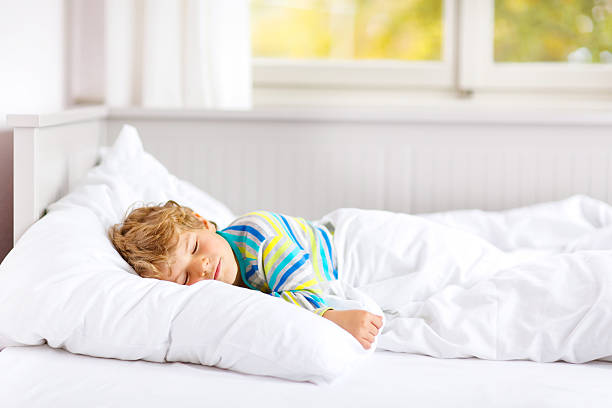 carefree little kid boy sleeping in bed in colorful nightwear. stock photo