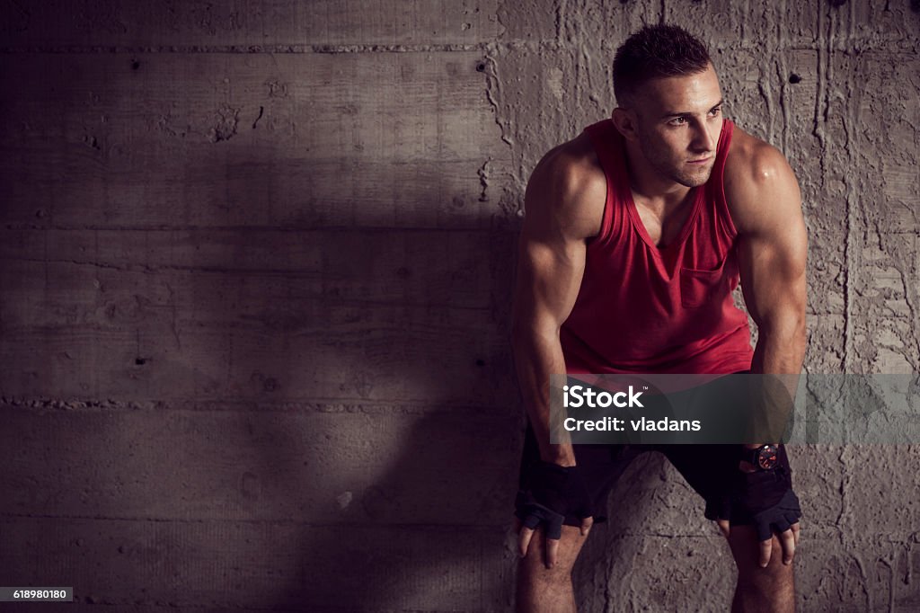 Workout break Muscular young athletic built sportsman, leaning against a concrete wall of an abandoned building, taking a break Men Stock Photo