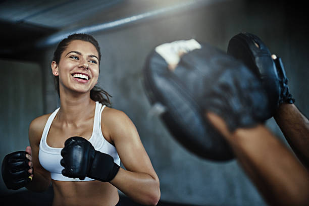 Boxing her way to a ripper body Shot of a young woman sparring with a boxing partner at the gym boxing sport stock pictures, royalty-free photos & images