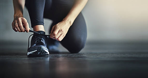 Potongan gambar seorang wanita mengikat tali sepatunya sebelum berolahraga