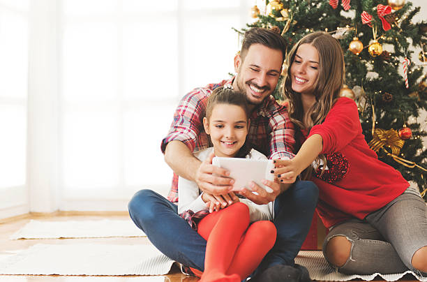 Family gathered around a Christmas tree, using a tablet