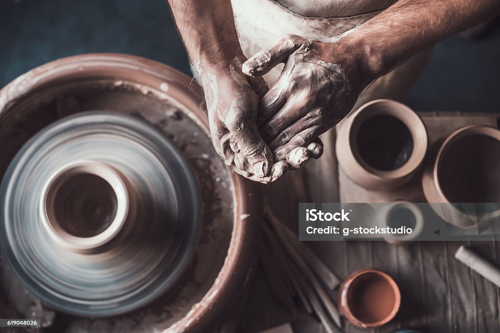 Potter at work. Top view of potter standing near pottery wheel and holding hands together Pottery Stock Photo