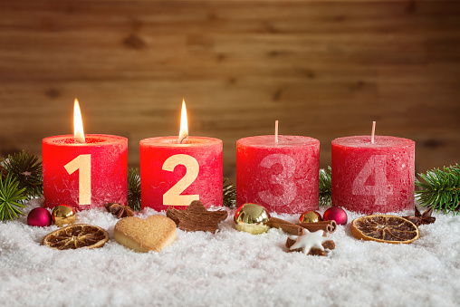 Four numbered red advent candles with two candles lit and christmas decoration lying in snow as template