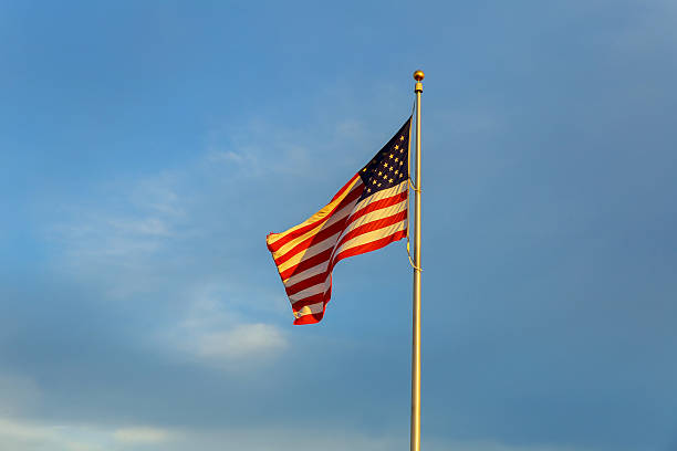 istock American flag on flagpole waving in the wind against clouds 619051900
