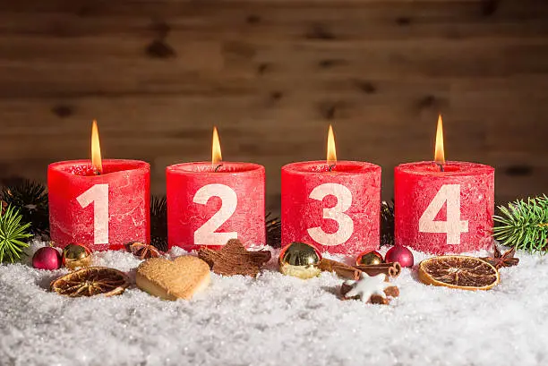 Four numbered red advent candles with four candles lit and christmas decoration lying in snow as template