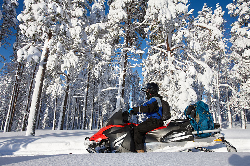 Man driving snowmobile in snowy forest in a sunny day. Lapland, Finland.