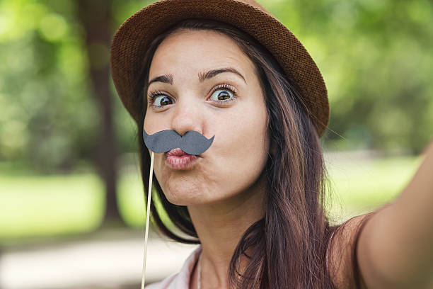 Mustache selfie Girl making a selfie with fake moustaches and grimacing in the park women movember mustache facial hair stock pictures, royalty-free photos & images