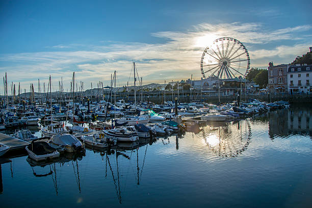 Torquay view at sunset Torquay, England - August 26, 2016: View of Torquay seafront, ferris wheel and boats reflecting in the water at sunset. People can be observed going about their business. torquay uk stock pictures, royalty-free photos & images