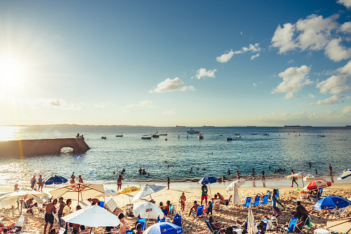 Salvador, Brazil - August 24, 2015: view on crowded summer evening beach Porto da Barra with of people relaxing under parasols and taking batch in the ocean