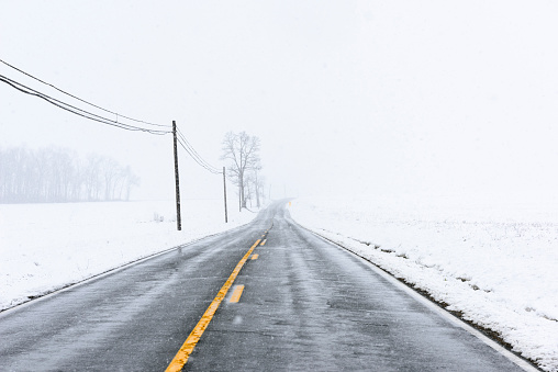 View of country road with telephone lines during a winter snow storm.