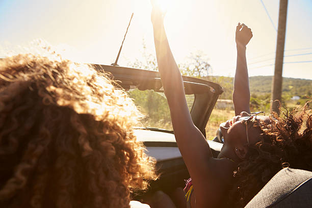 pareja joven en un coche des abierto, mujer con los brazos en alto - couple young adult african descent multi ethnic group fotografías e imágenes de stock