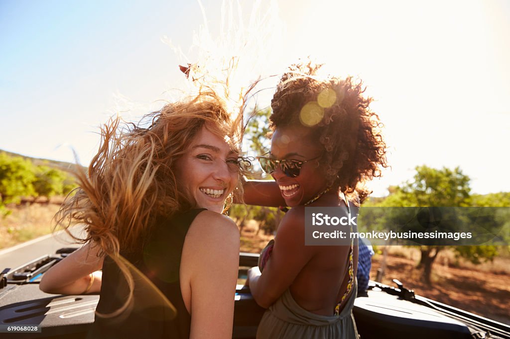 Two women standing in the back of open car turning Two women standing in the back of open car turning to camera Friendship Stock Photo