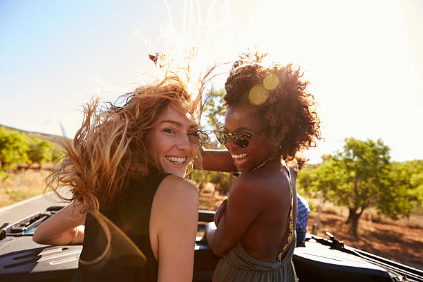 Two women standing in the back of open car turning Two women standing in the back of open car turning to camera friends laughing stock pictures, royalty-free photos & images