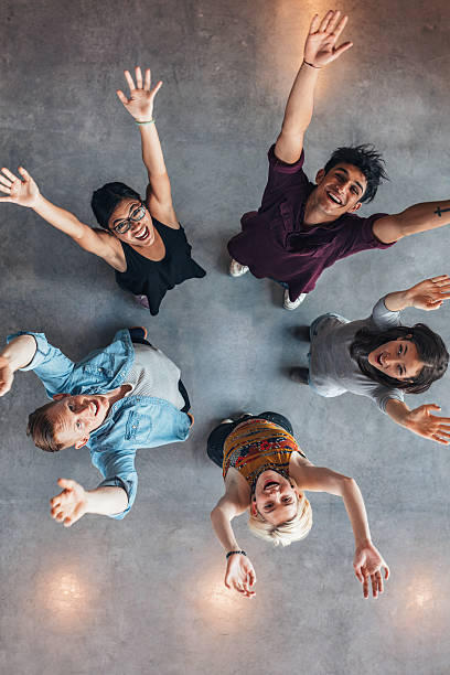 University students cheering Overhead view of young people standing together looking up at camera with their arms raised. University students cheering. cheering group of people success looking at camera stock pictures, royalty-free photos & images