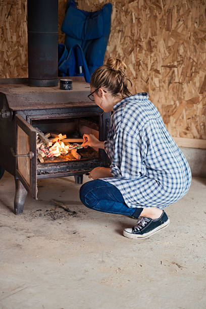 istock Young woman lighting a fire in a shed fireplace. 619069192