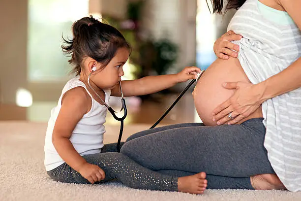 Photo of Young ethnic girl putting stethescope to pregnant moms belly