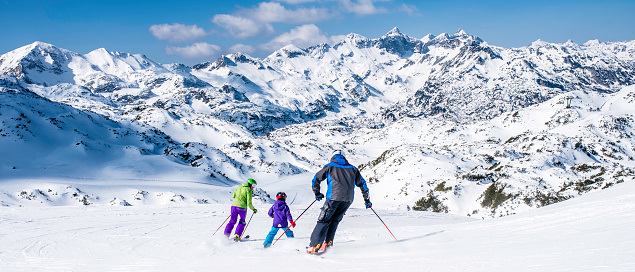 Back view of a family with one child on ski slope.