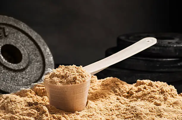 Product photograph of spoon or measuring scoop of whey protein on black chalkboard background