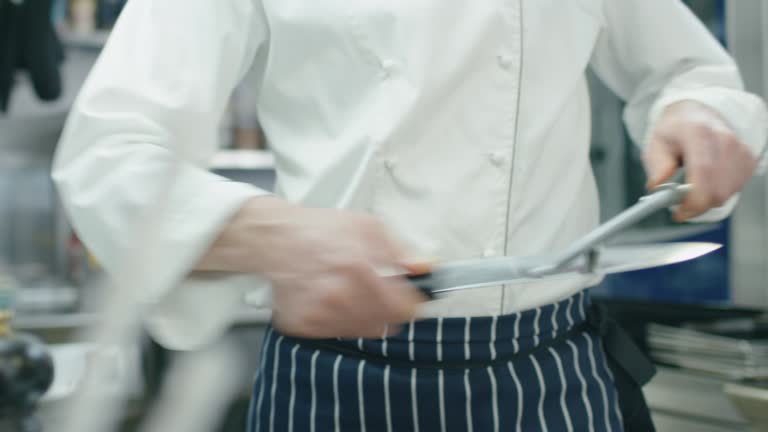 Professional chef in a commercial kitchen in a restaurant or hotel is sharpening knifes.