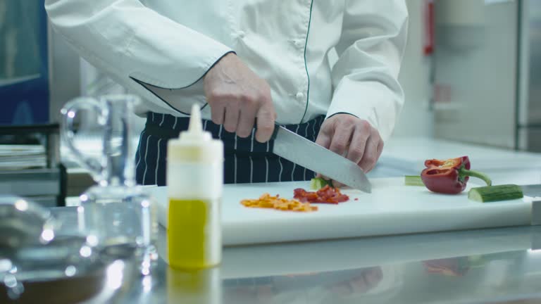 Professional chef in a commercial kitchen is slicing green vegetables.