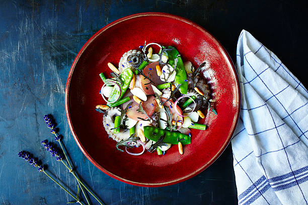 Octopus Salad Octopus salad with green beans and onion. Red plate standing on the middle of the frame. Surface is a dark blue metal surface with a cloth on side. food styling stock pictures, royalty-free photos & images