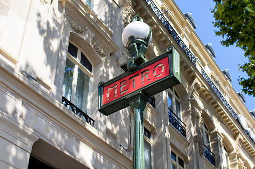 Traditional metro sign with old, historical building in the background in Paris.
