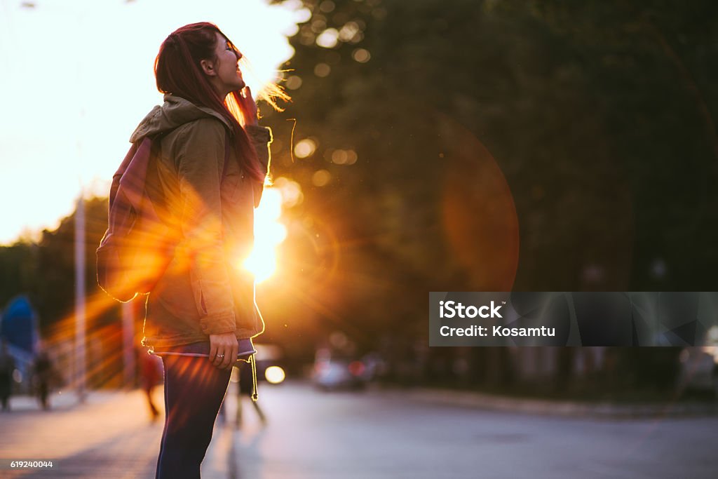 Redheaded Beauty in Sunset Smiling Young Red-haired woman dressed in jacket is enjoying vivid sunset in the streets. Winter Stock Photo