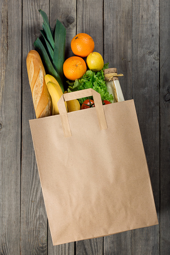 Various food in paper bag on wooden background. Grocery shopping concept, top view