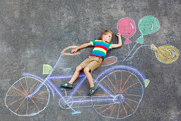 istock little kid boy drawing bicycle chalks picture on ground 619244726