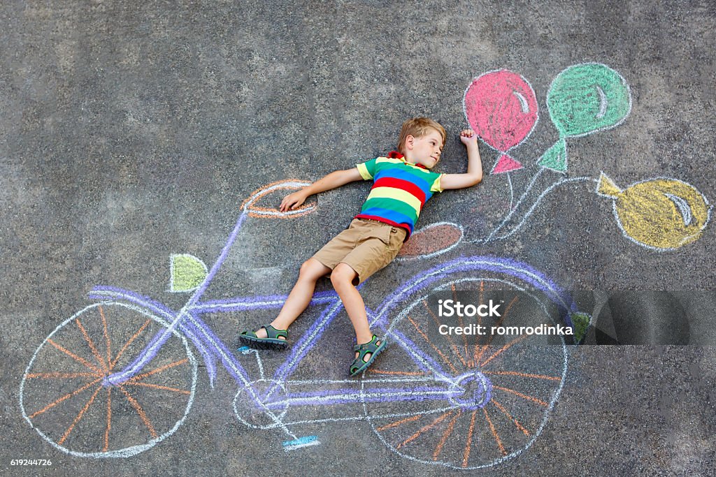 little kid boy drawing bicycle chalks picture on ground Happy little kid boy having fun with bicycle and air balloons picture drawing with colorful chalks on ground. Children, lifestyle, fun concept. funny child playing and dreaming of future and profession. 4-5 Years Stock Photo