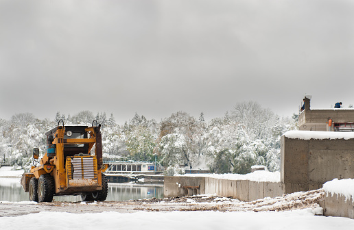 little yellow tractor bulldozer builds the building in the winter on a background of lake