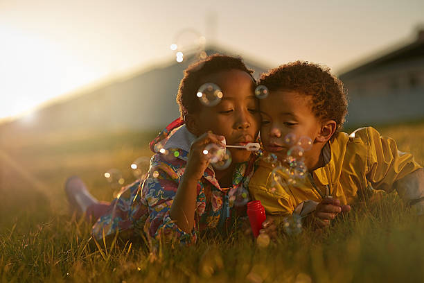Siblings and the best of friends Shot of a brother and sister lying on the ground outside blowing bubbles brother stock pictures, royalty-free photos & images
