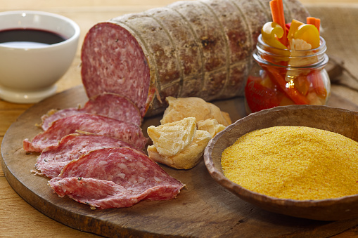 A composition of traditional Northern Italy food: sopressa, pickels,, corn powder and red wine