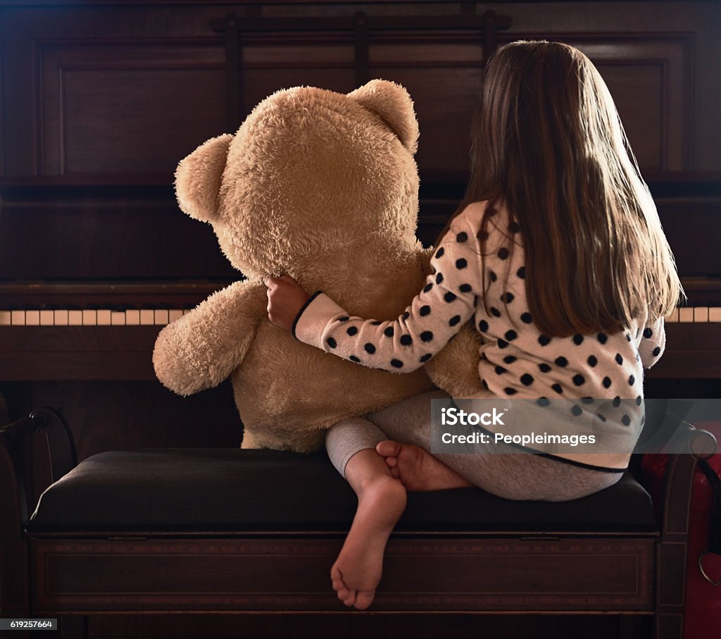Sharing her talents with her teddy Rear view shot of a little girl sitting in front of a piano with her teddy bear Brown Hair Stock Photo
